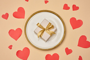 A gift with a gold bow on a plate surrounded by red hearts on a, a Holiday Photo by ndanko