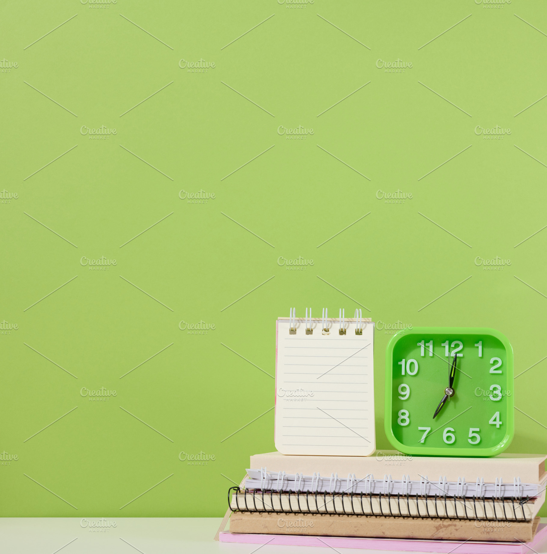 An open notepad and a green alarm clock stands on a stack of not, an Abstract Photo by ndanko
