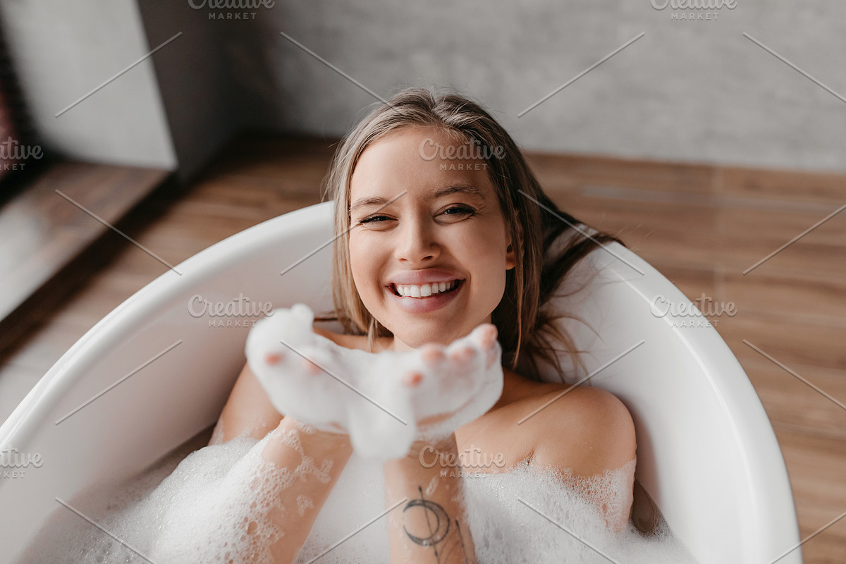 Playful lady having fun while lying in bathtub full of foam, blowing soap bubbl, a Photo by Prostock-Studio (Photo 1 of 4)