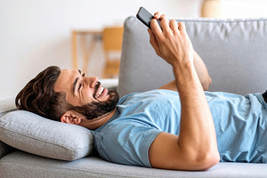 Smiling Man Relaxing with Smartphone on Sofa, a Photo by Davizro's Market