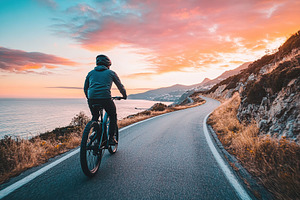 Man enjoys a coastal ride on an electric bike during a stunning sunset, a Sports & Recreation Photo by AlyaAnd