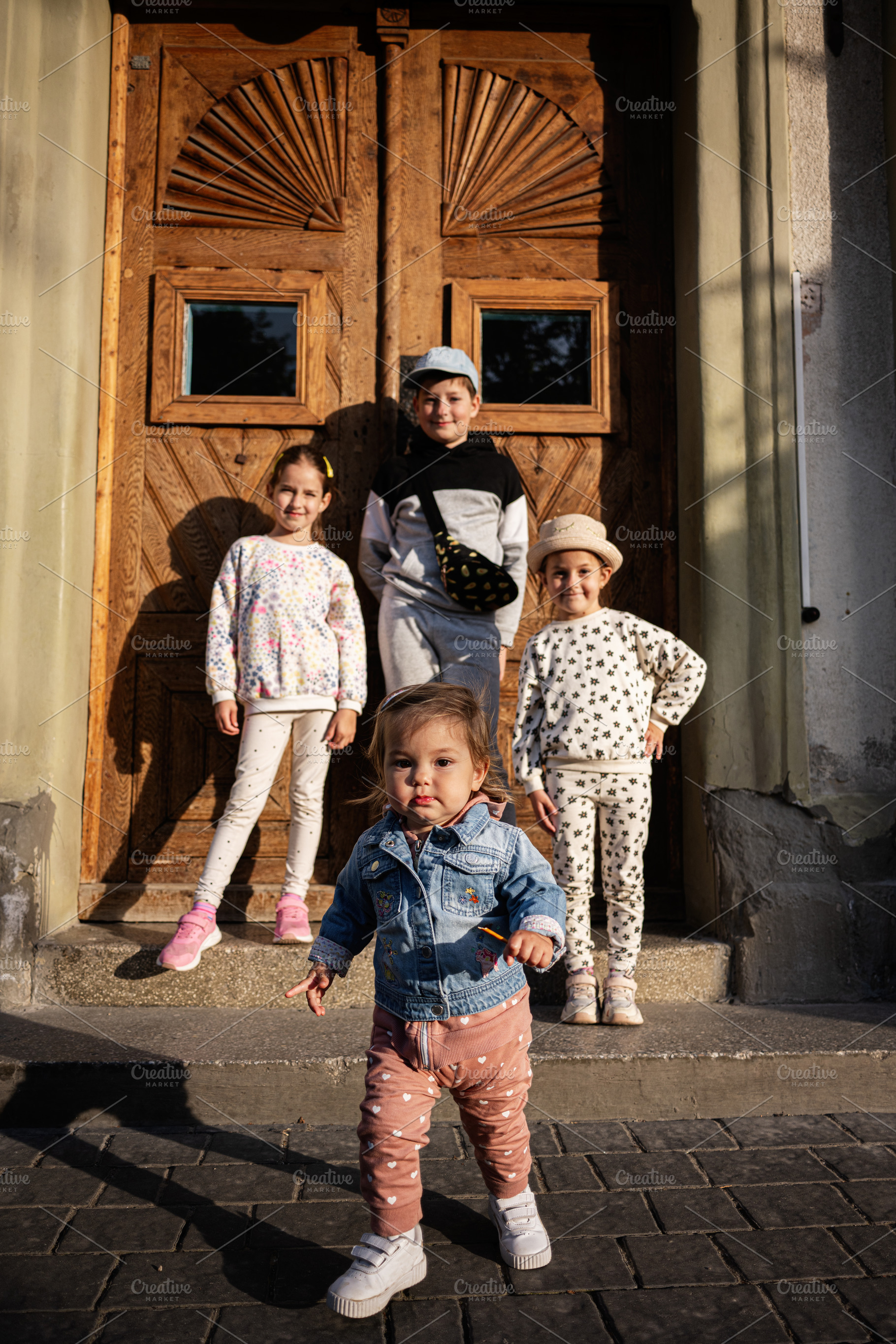 Group of four children posing outdoors on a sunny day by a wooden door, a Person Photo by AS photostudio