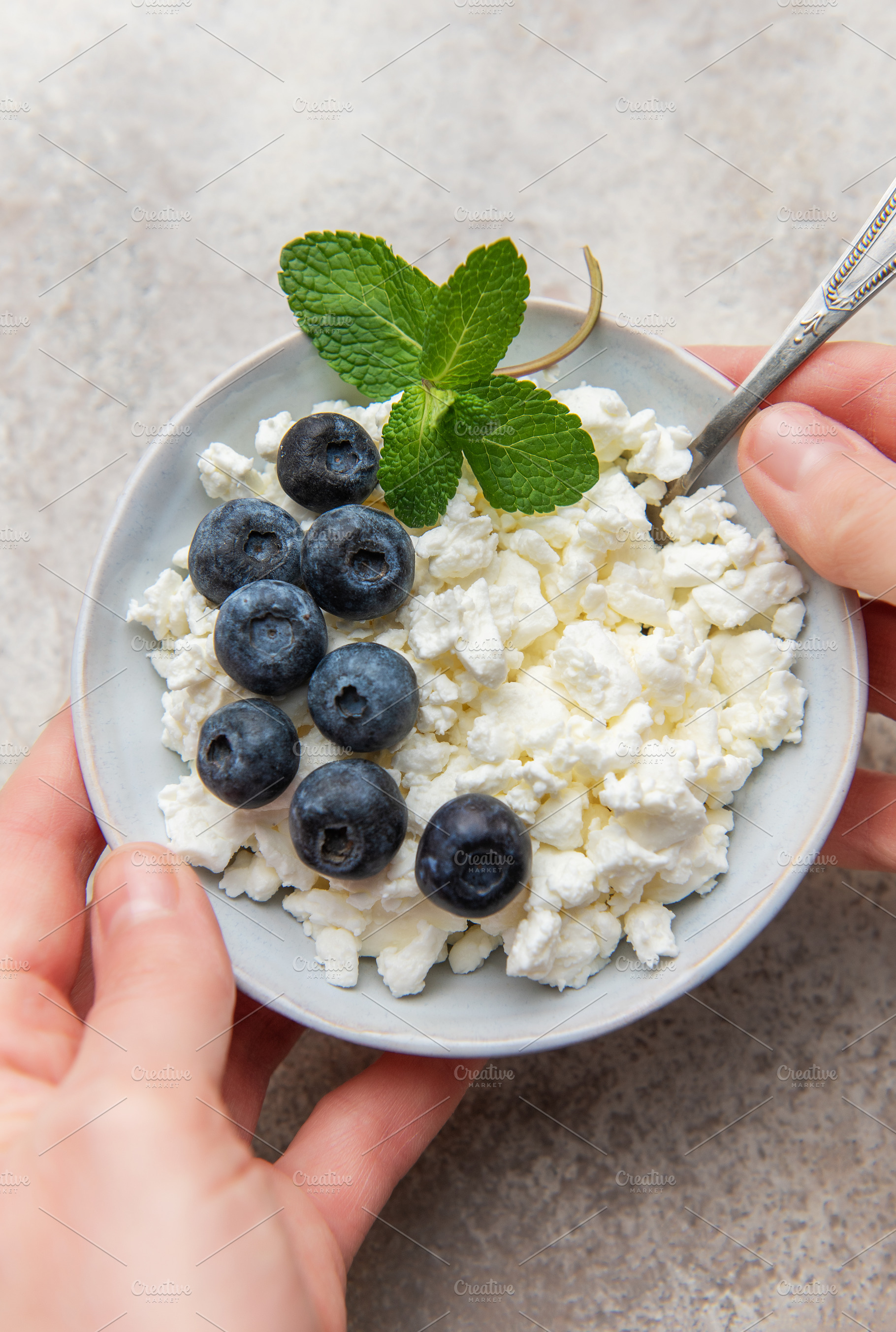 Hands holding a bowl of cottage cheese with blueberries and mint, a Food & Drink Photo by Olena Rudo