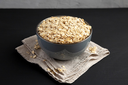 Wholegrain Oat Flakes in a Bowl on a black background, side view, a Food & Drink Photo by LiudmylaChuhunova