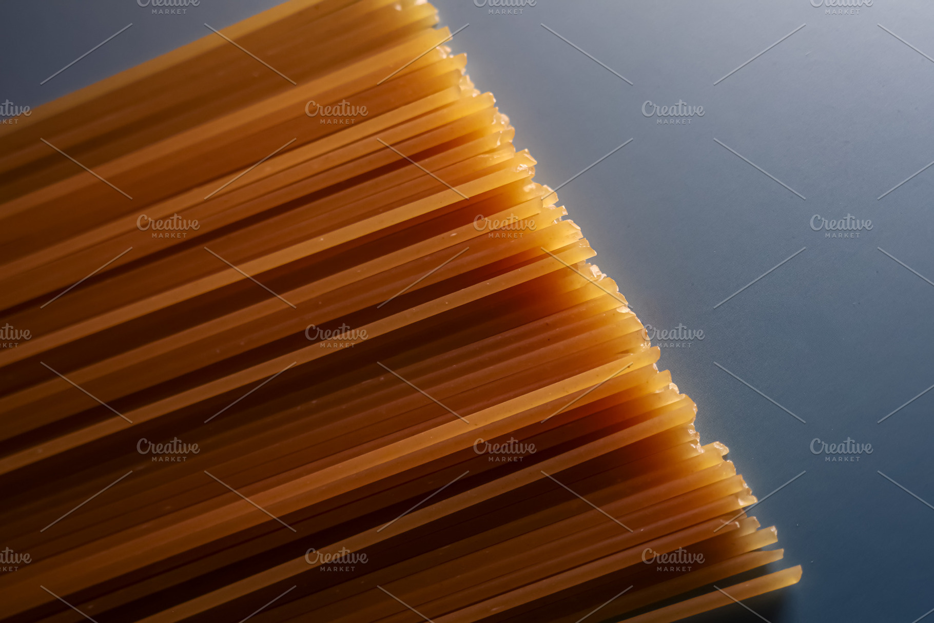 Dry spaghetti pasta strands forming a diagonal pattern on a grey background, cr, a Photo by Studio ANNA