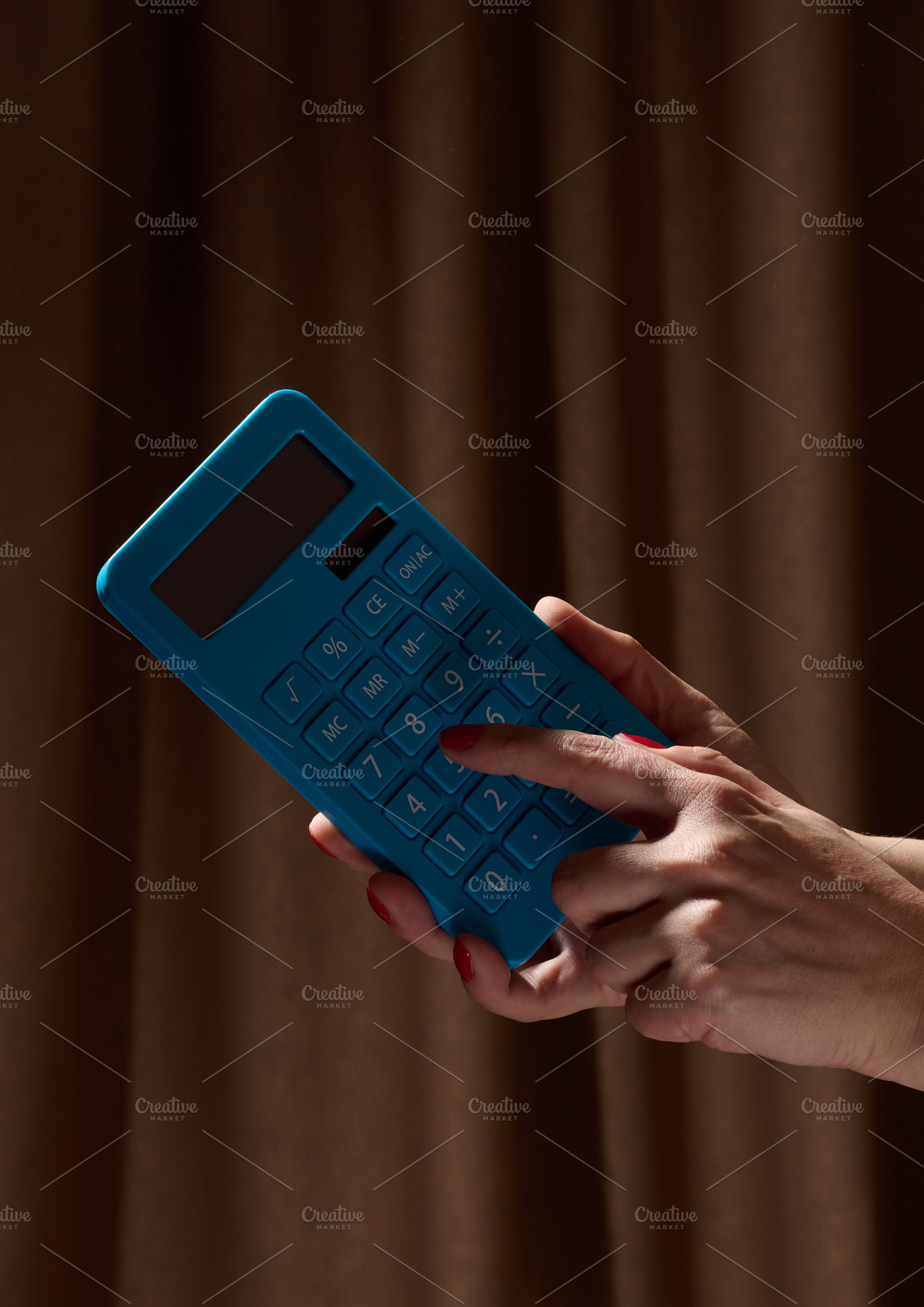 A person calculating on a blue calculator against a dark backgro, a Business Photo by ndanko