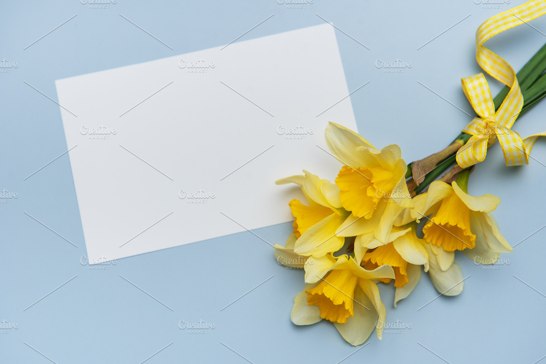 Bouquet of daffodils with greeting card lying on blue table, a Nature Photo by Olena Rudo