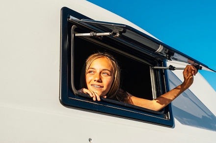 The happy girl sticks her head out of the van window on a wonderful day at camp, a Person Photo by karrastock