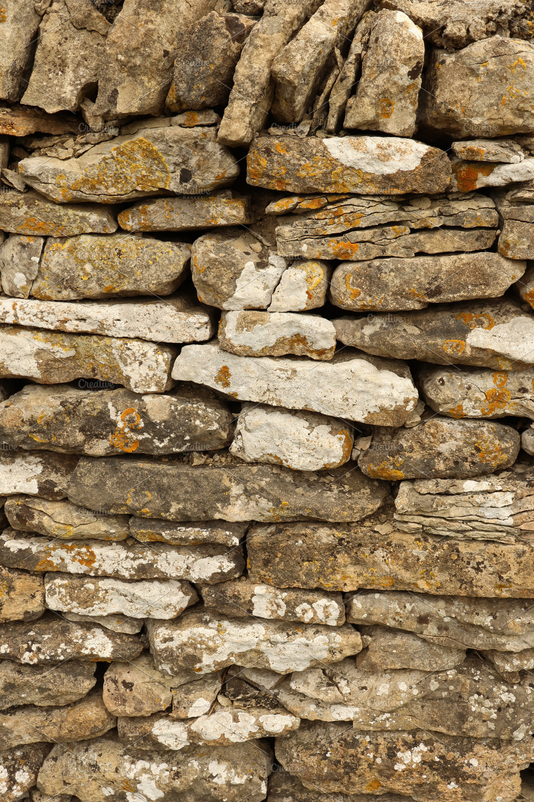 Dry stone wall texture showing stacked rocks with lichen and mos, a Photo by Studio ANNA