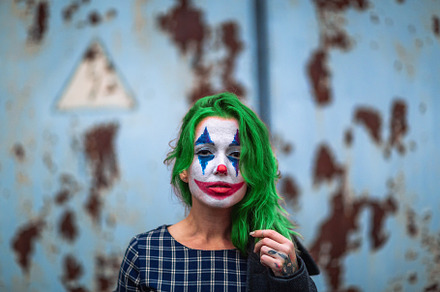 Portrait of a greenhaired girl in chekered dress with joker makeup on a rusty m