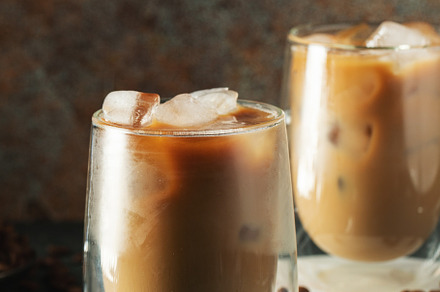 Ice coffee in a tall glass with cream poured over, ice cubes and beans on a dar, a Food & Drink Photo by Budarinphoto