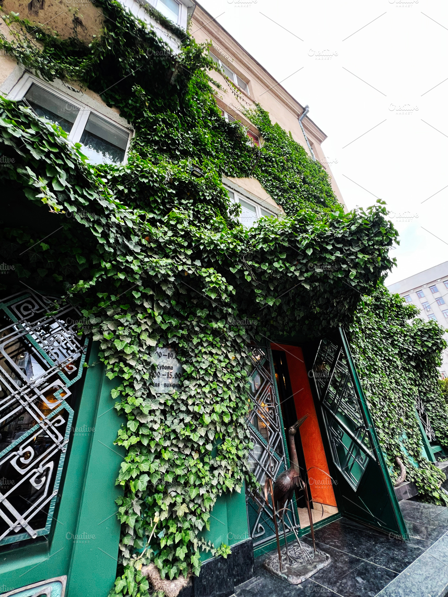 Building exterior covered with lush greenery featuring intricate door design an, a Photo by AS photostudio