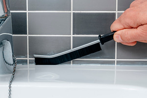 a man scrubs the joints along the sink tiles, a Photo by Nito
