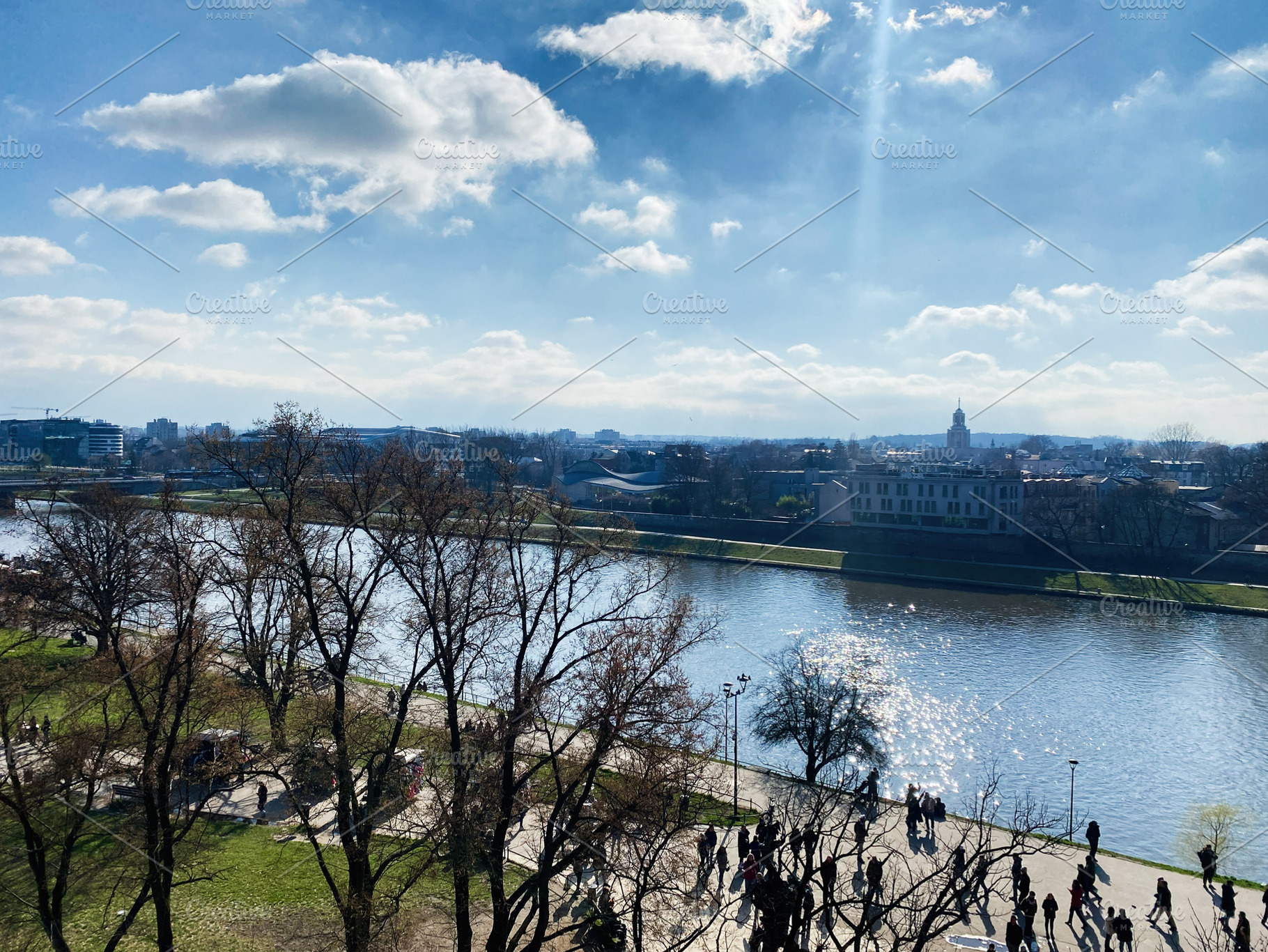 Sunny riverside with trees and people in Krakow, Poland under blue sky, a Photo by AS photostudio