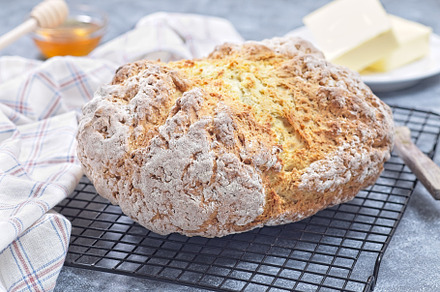 Freshly baked soda bread on cooling rack with butter and honey in the backgroun