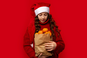 Girl in Santa hat holds paper bag, a Person Photo by Elena Vagengeim