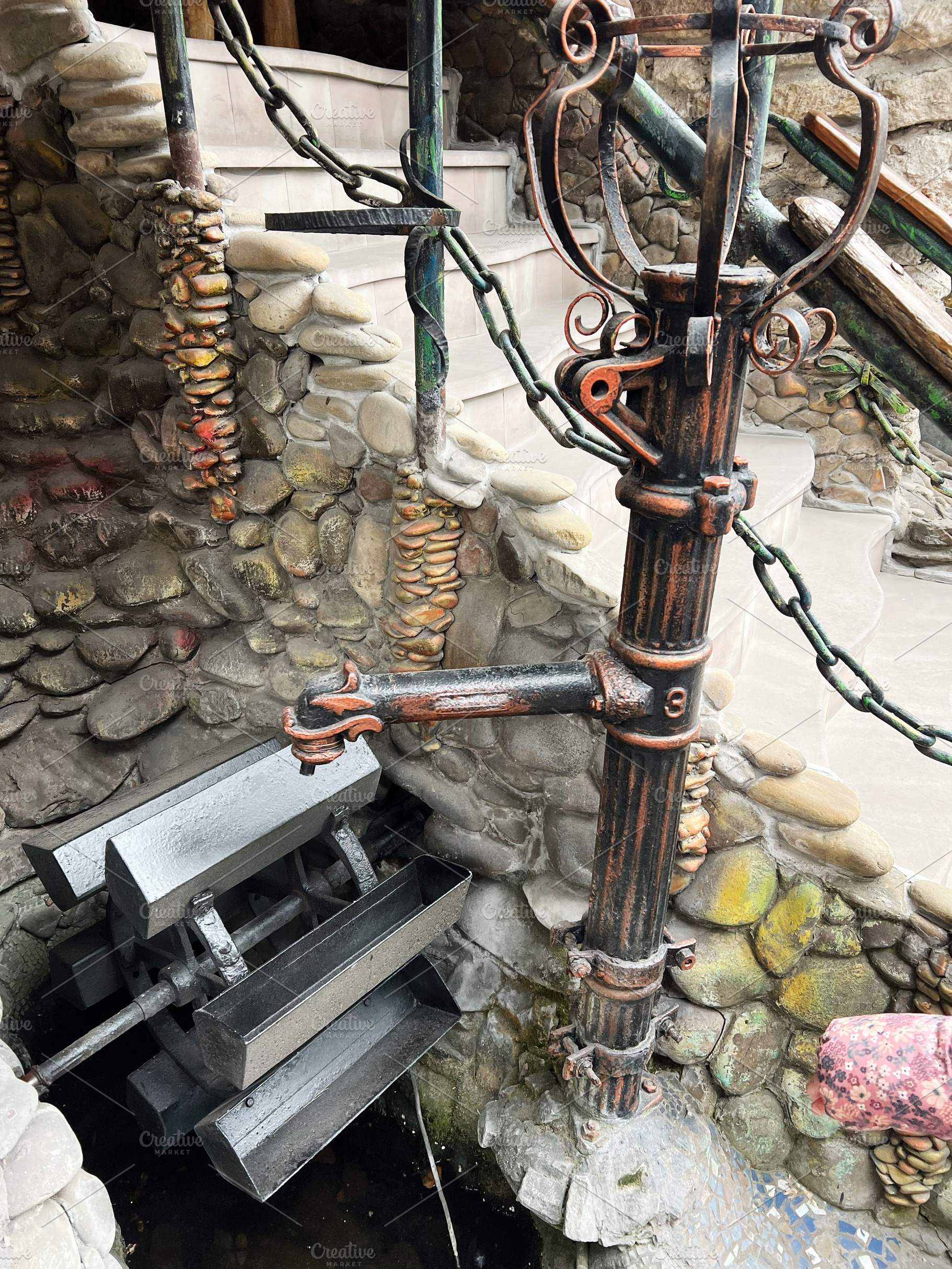 Ornate old pipe and water wheel in a rustic stone setting, a Photo by AS photostudio