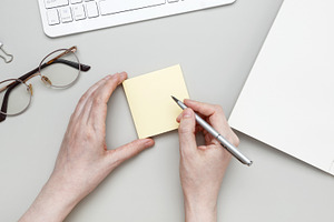 At tidy workspace, woman jots notes on sticky pad surrounded by notebook and st, a Photo by matucha