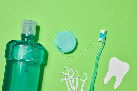 Green toothbrush, mouthwash bottle, dental floss in case, plasti