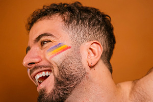 Happy man celebrating pride with rainbow face paint, a Photo by karrastock