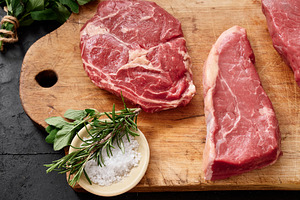 Raw rib-eye, roast beef, flank, and rump steak placed on a wooden cutting board