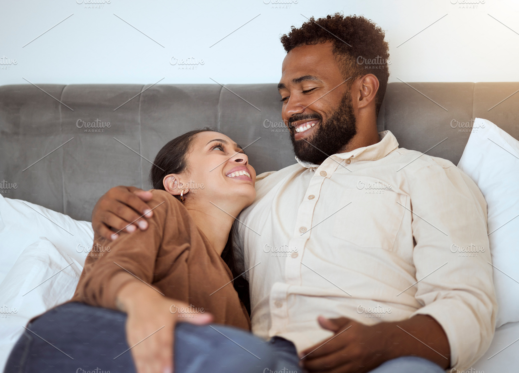 Love, relax and couple in bed in their home, resting and smiling while talking and bonding in bedroom together. Black family, resting and comfort with smile, happy and laughing man and woman embrace, a Photo by Peopleimages.com