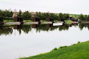 Row of outdoor huts reflected on a calm lake surface on a cloudy day, a Photo by AS photostudio