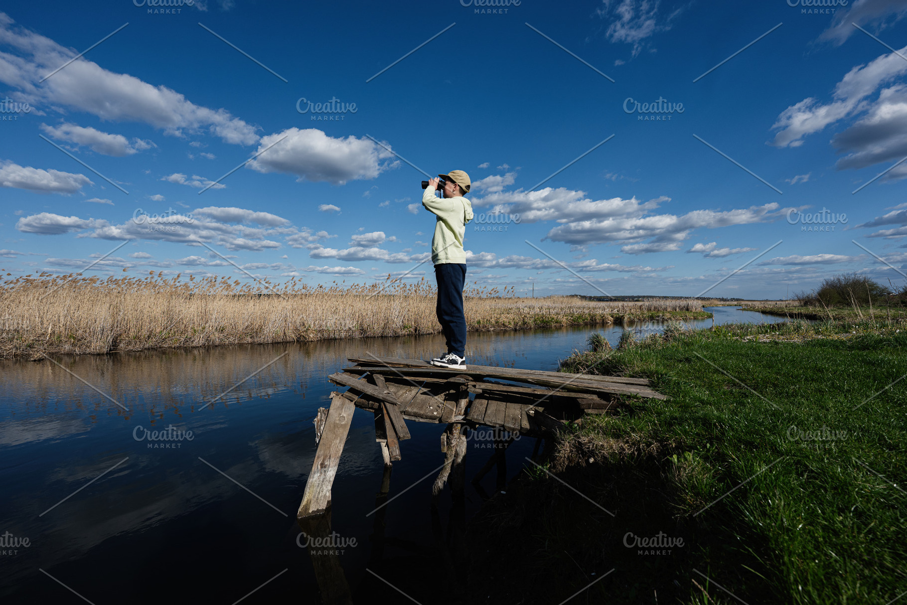 Young person observing marshland with binoculars from a rickety wooden dock und, a Person Photo by AS photostudio