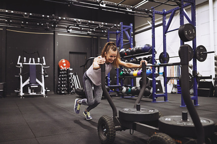 Smiling mature woman pushing a sled during a gym workout