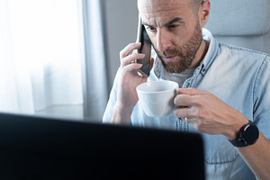 Businessman talking on smartphone while drinking coffee at home office, a Person Photo by etorres69