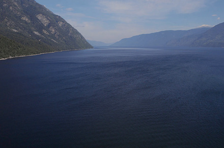 Lake Teletskoye between mountains with blue clear sky in Altai, a Nature Photo by TravelFlow