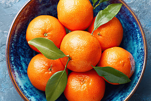 Fresh tangerines arranged in a decorative bowl with leaves, a Photo by AlyaAnd