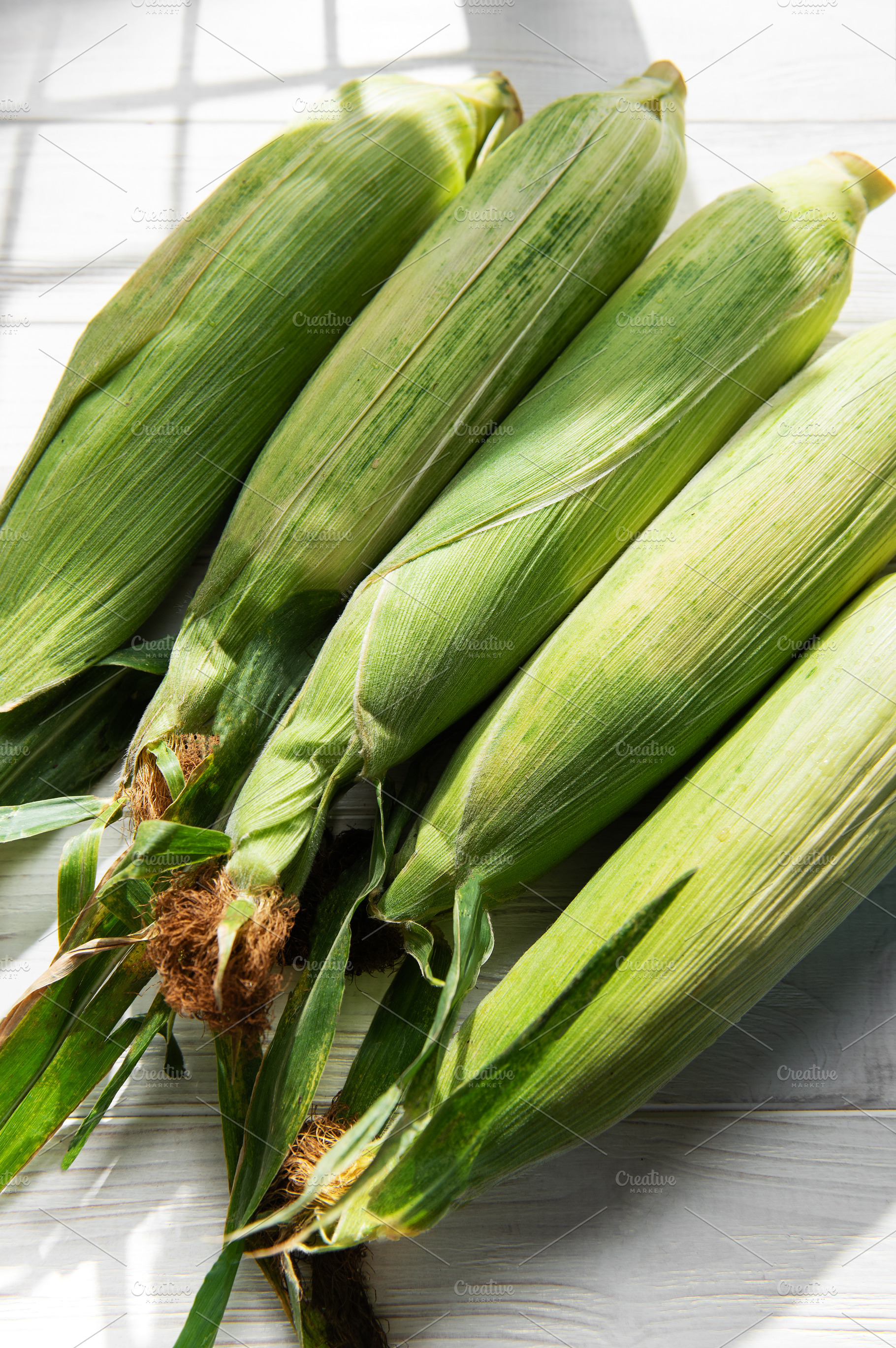 Fresh corn cobs on white wooden table, a Food & Drink Photo by Olena Rudo