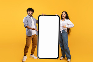 Cool mobile offer. Happy indian couple pointing at big cellphone with white scr, a Person Photo by Prostock-Studio