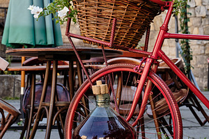 Red vintage bicycle with flower basket and large wine demijohn on a rustic cafe, a Nature Photo by Rohan Photography