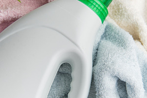 Laundry detergent bottle resting on clean towels and tropical le, an Industrial Photo by Olena Rudo