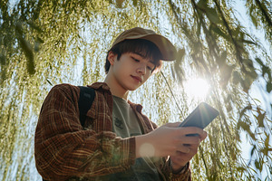 A young person wearing a cap and a plaid shirt is standing under a willow tree,, a Technology Photo by Textures & Backgrounds