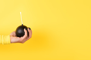 A female hand in a yellow sleeve holds a round black cartoon bom, a Person Photo by Ales Munt