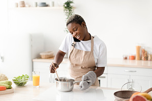 Happy young african american lady in apron prepare food, talk by phone communic, a Person Photo by Prostock-Studio