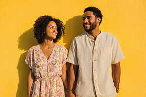 Young couple smiling together against a bright yellow background in a sunny loc, a Person Photo by AlyaAnd