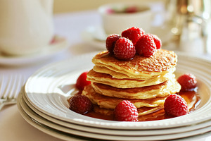 Stack of golden pancakes dripping with maple syrup, topped with fresh red raspb, a Photo by Studio ANNA