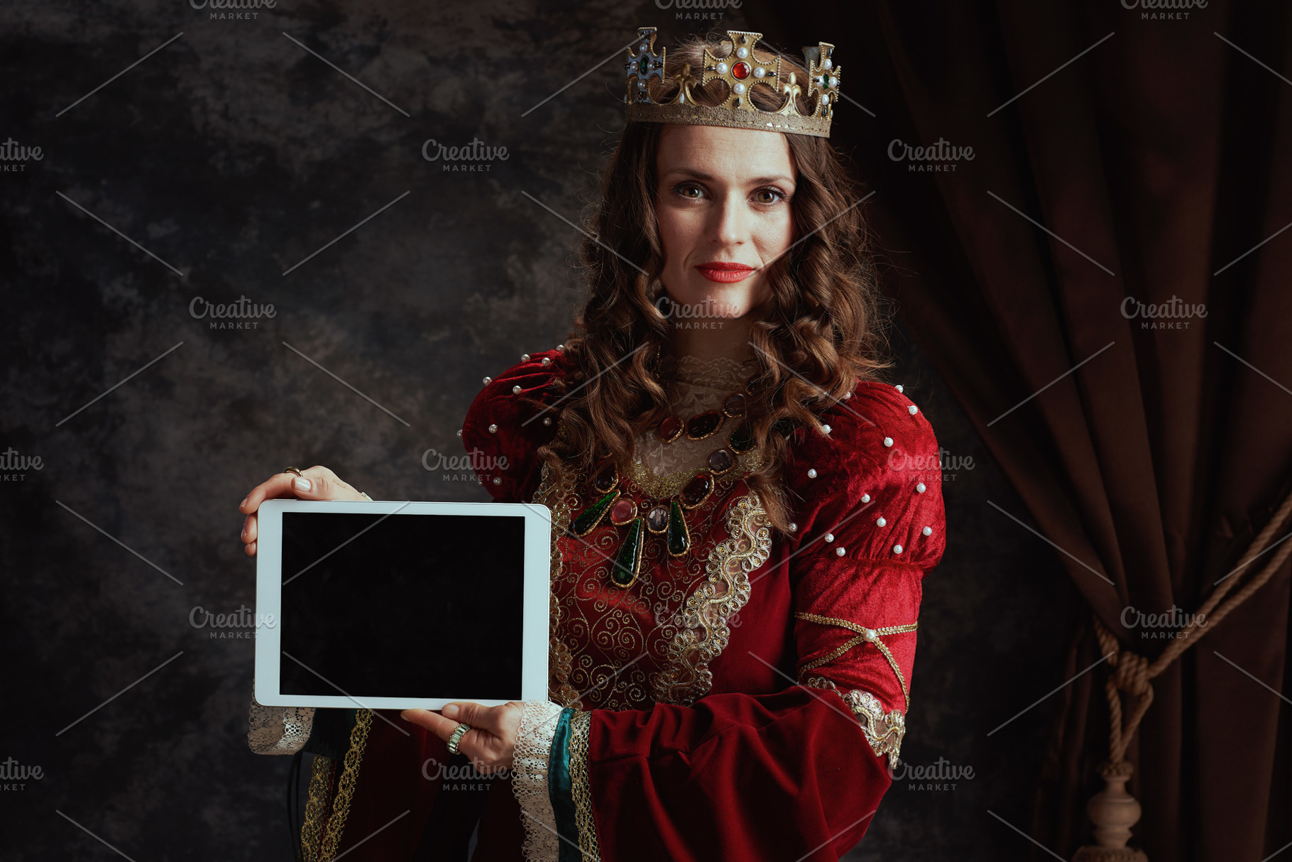 medieval queen in red dress showing tablet PC blank screen, a Person Photo by Alliance Images