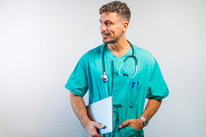 Male doctor holding a tablet and looking to the side, dressed in green scrubs w, a Person Photo by karrastock