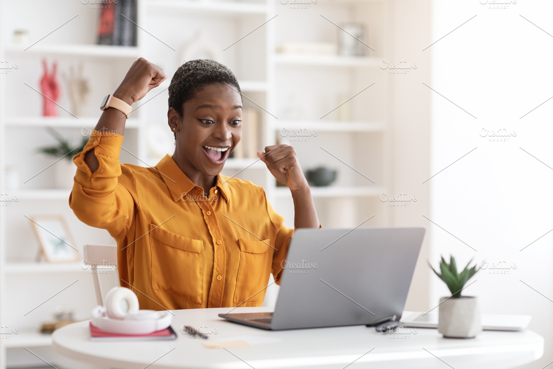 Emotional african american businesswoman celebrating success, working on laptop, a Photo by Prostock-Studio