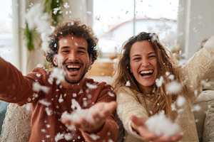 Joyful couple playing with fluff from the pillow indoors, a Person Photo by AlyaAnd