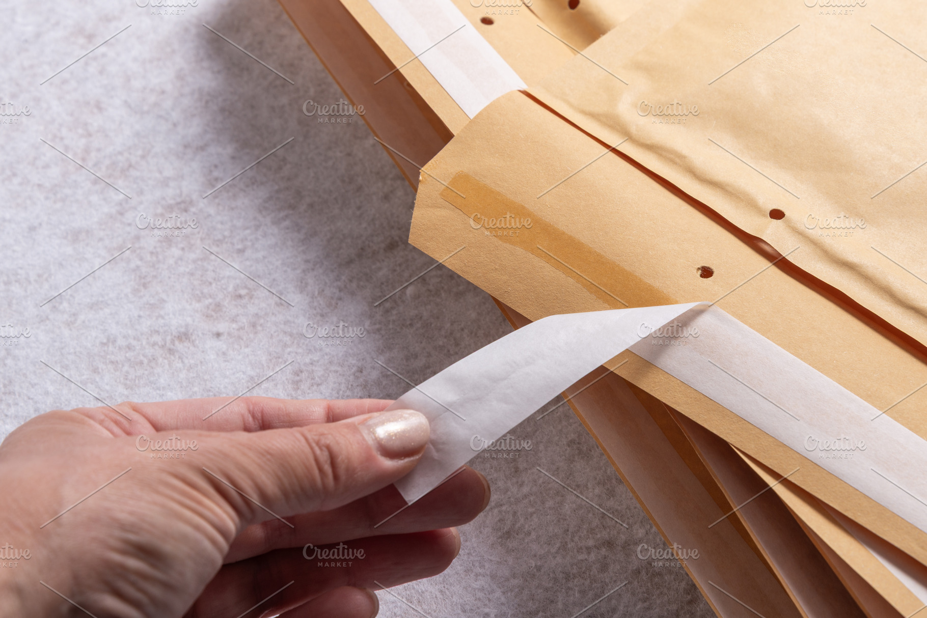 Female Hand Peeling Adhesive Tape on Bubble Mailer Plastic Padde, an Industrial Photo by MDBildes