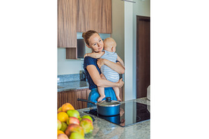 Mother holding baby while cooking, a Food & Drink Photo by Elizaveta Galitskaya