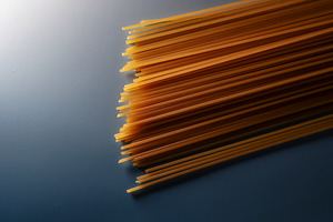 Uncooked whole wheat spaghetti noodles on a blue surface, prepar, a Photo by Studio ANNA