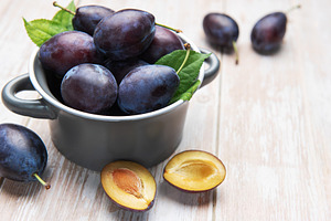 Fresh ripe plums in bowl on wooden table, a Food & Drink Photo by Olena Rudo