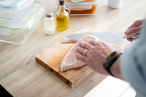 Man Cutting Raw Chicken Breast in Home Kitchen, a Food & Drink Photo by etorres69
